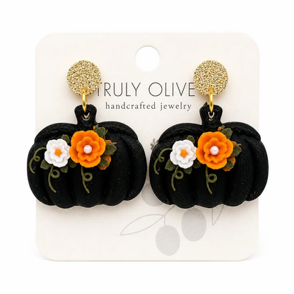 Handcrafted black pumpkin floral earrings with orange and white flowers, green vine accents, and textured gold stud tops on a clean boutique background.