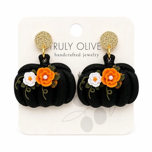 Handcrafted black pumpkin floral earrings with orange and white flowers, green vine accents, and textured gold stud tops on a clean boutique background.