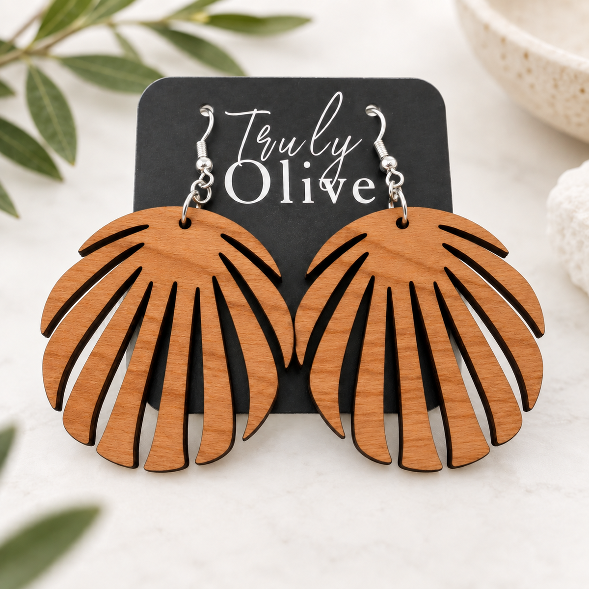 Cherry wood leaf earrings on a Truly Olive card, styled on cream linen with softly blurred greenery.