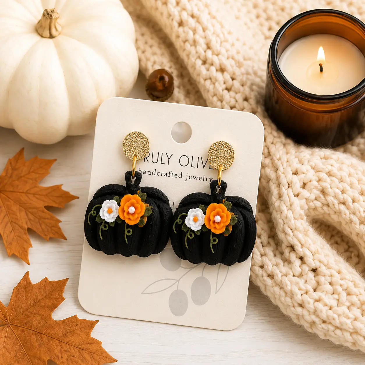 Lay-flat display of black pumpkin earrings with orange and white flowers, green vine details, and gold studs styled with autumn accents.