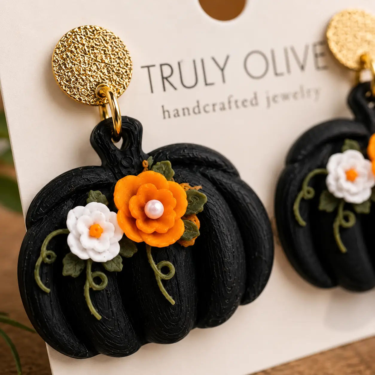 Close-up of handcrafted black pumpkin earrings showing textured pumpkin ridges, dimensional flowers, delicate green vines, and gold-tone hardware.