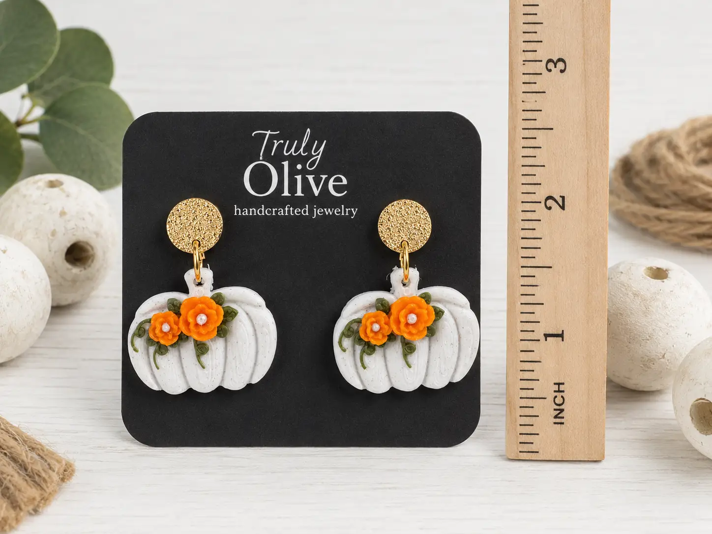 Size comparison of black pumpkin dangle earrings with orange and white floral accents, showing the approximate length and width.
