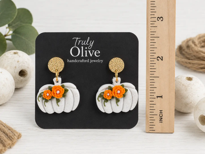 Size comparison of black pumpkin dangle earrings with orange and white floral accents, showing the approximate length and width.
