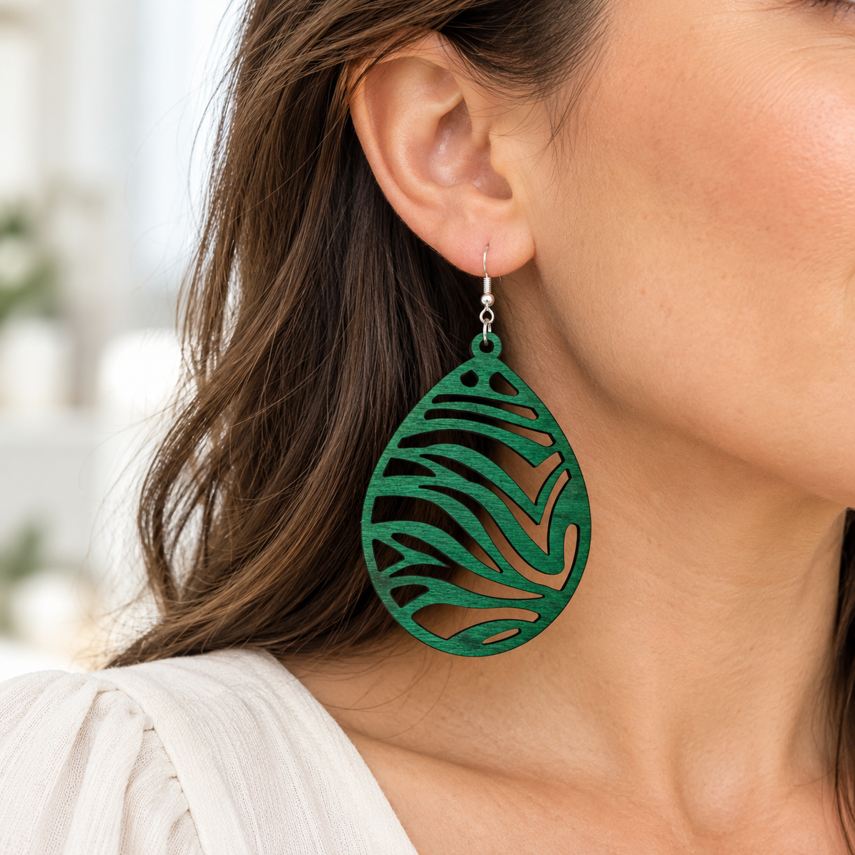 Close-up of a model wearing a Green wood teardrop earring with zebra cutouts, styled with a cream blouse.