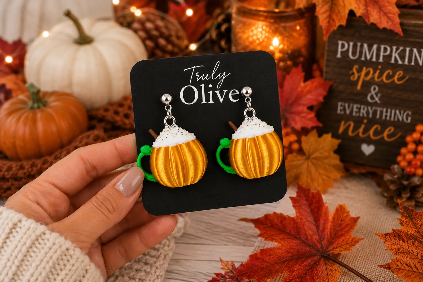 Close-up of handcrafted pumpkin spice mug earrings held in hand, highlighting detailed whipped cream, cinnamon stick, and pumpkin mug design.