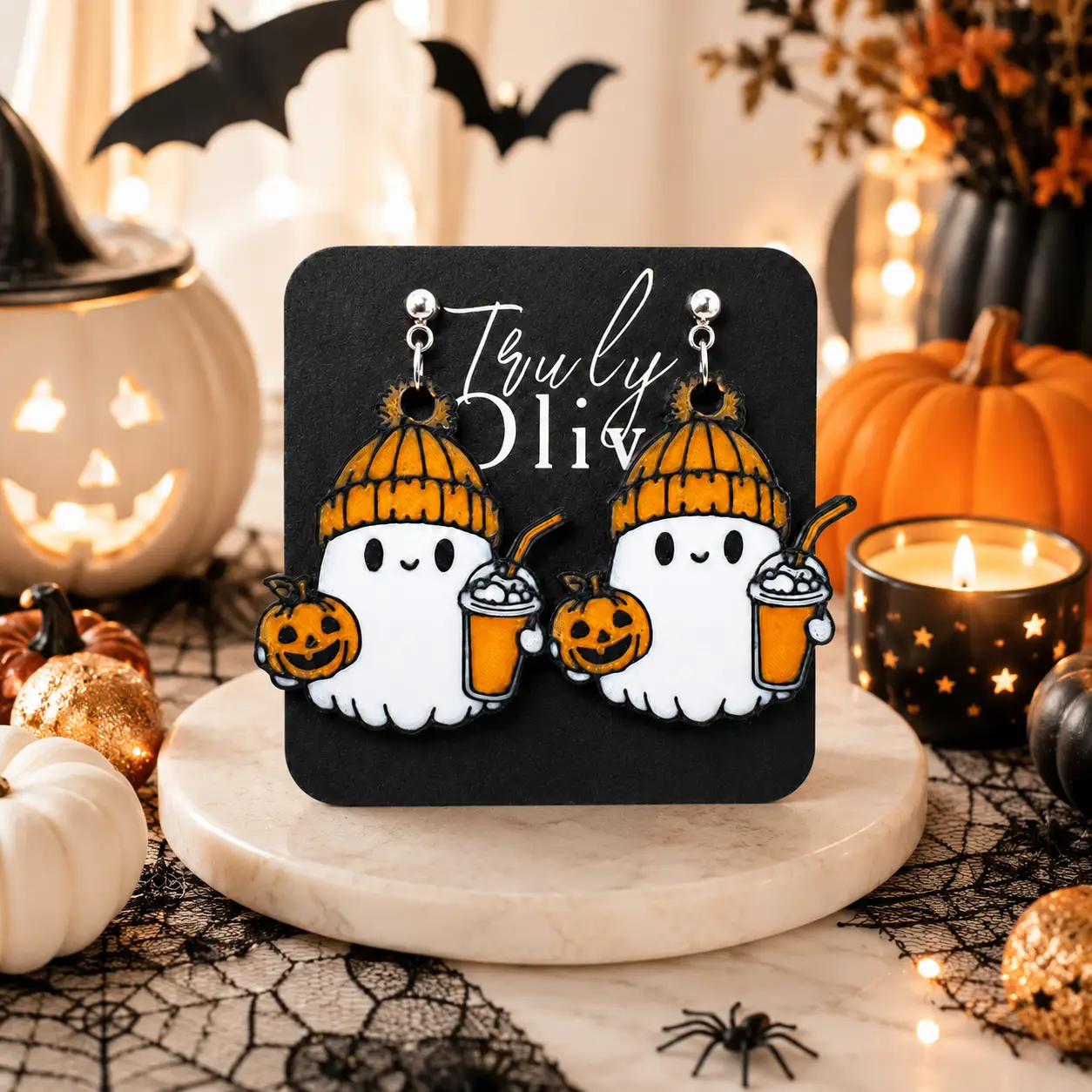 Close-up of cozy ghost Halloween earrings on a black Truly Olive card, highlighting the printed texture, orange hats, jack-o’-lanterns, festive drinks, and polished silver hardware.