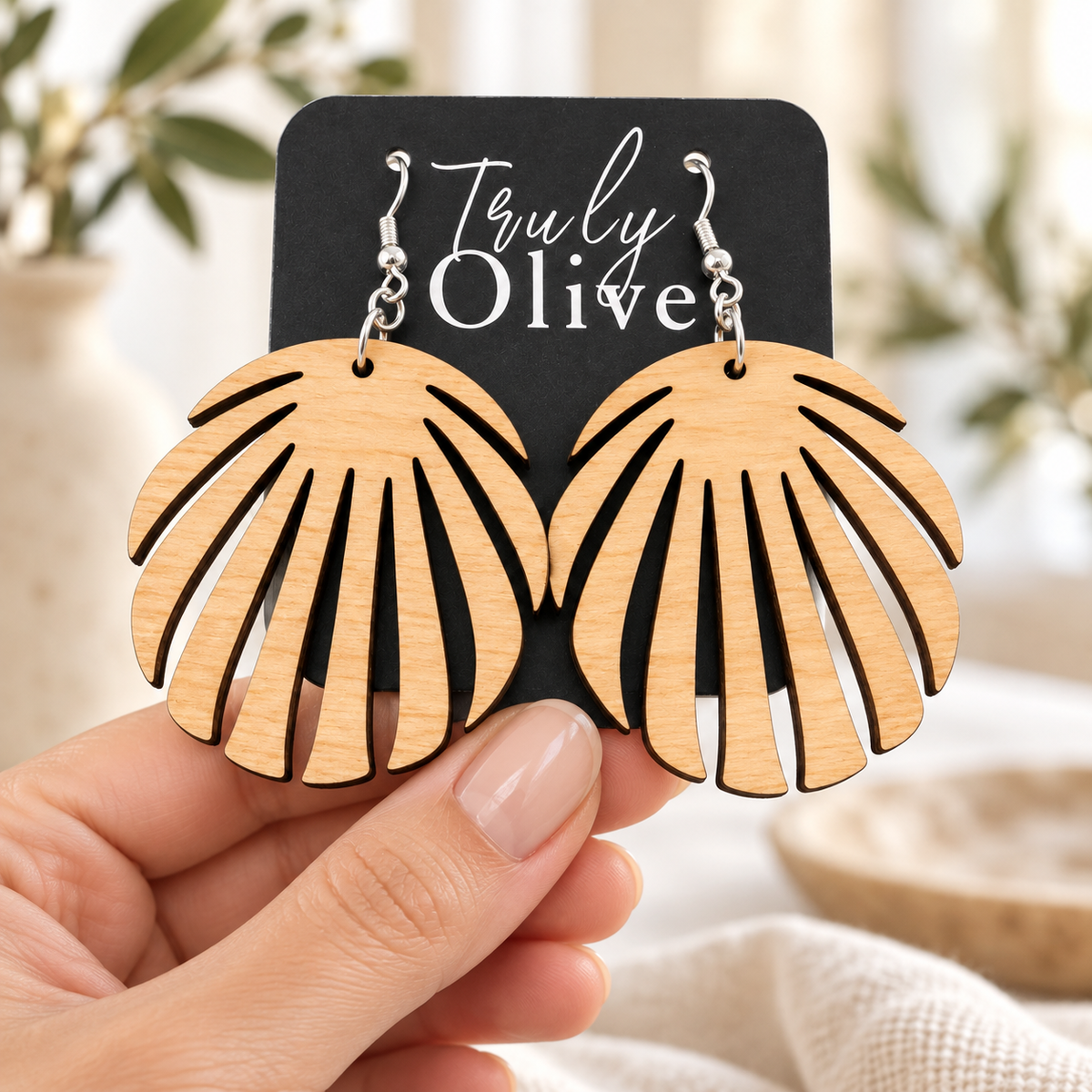 A hand holds the Truly Olive card displaying a pair of Maple wood leaf earrings.