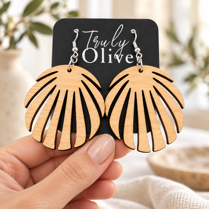 A hand holds the Truly Olive card displaying a pair of Maple wood leaf earrings.