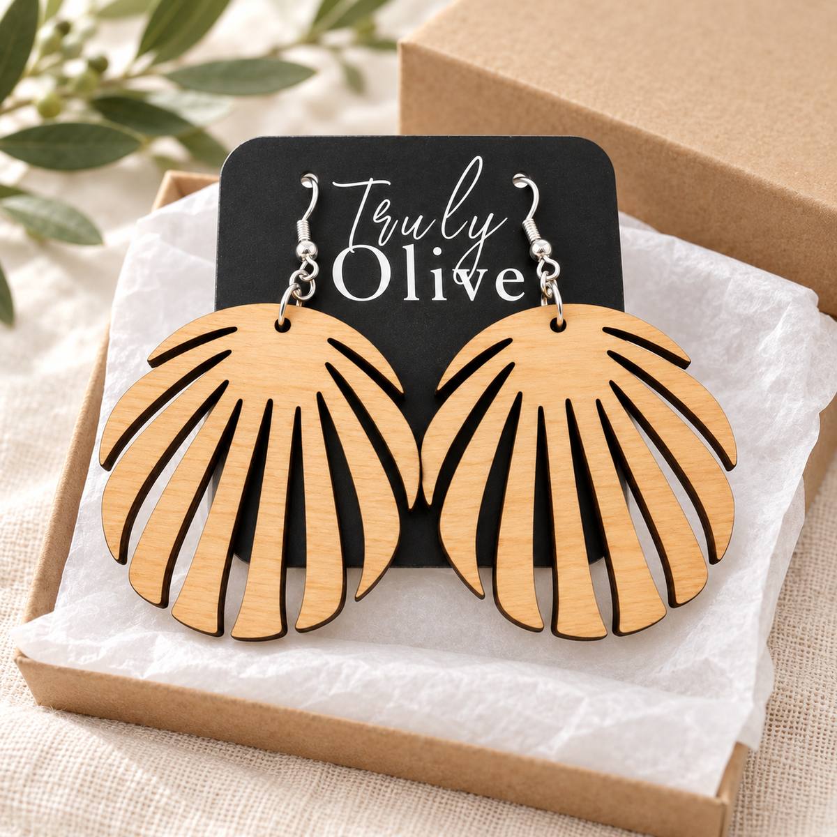 Maple leaf earrings on a Truly Olive card resting in a tissue-lined kraft box.