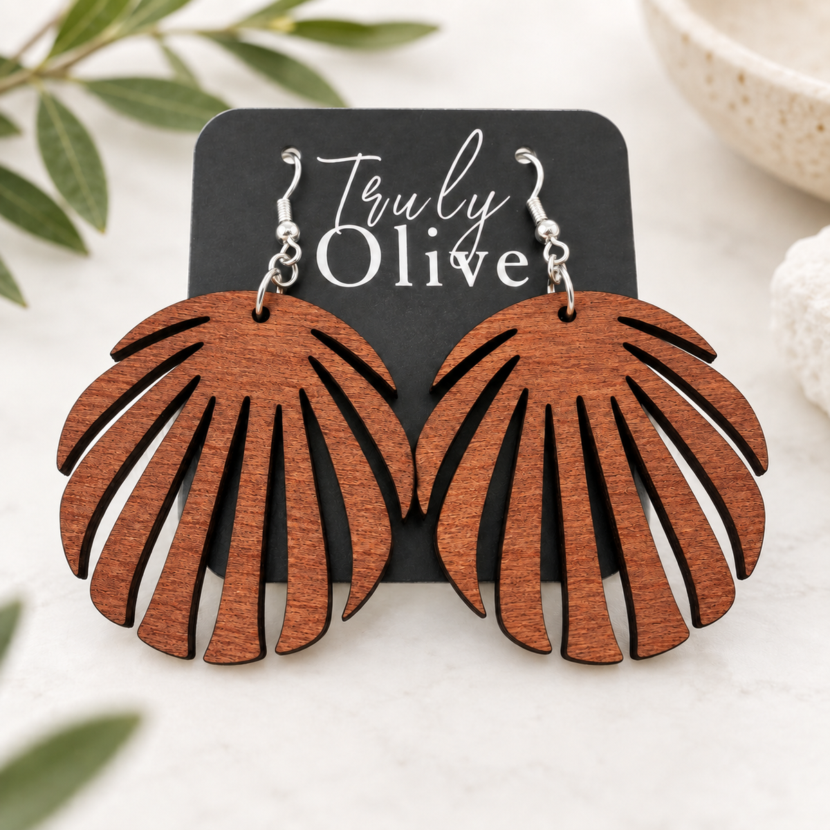 Sapele wood leaf earrings on a Truly Olive card, styled on cream linen with softly blurred greenery.