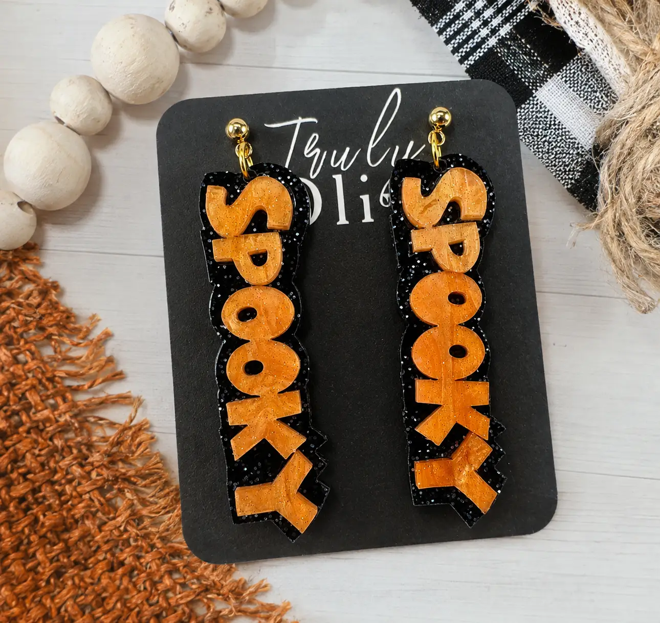 Long SPOOKY earrings styled in a festive Halloween setting with pumpkins, spiderwebs, candles, bats, and warm orange lighting.