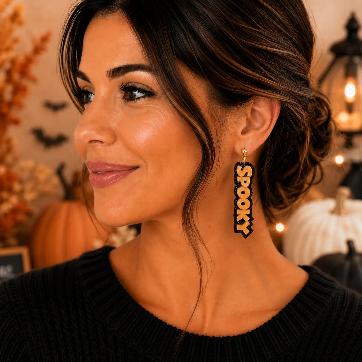 Model wearing long orange SPOOKY Halloween earrings with black glitter lettering and gold-tone hardware in a festive seasonal setting.