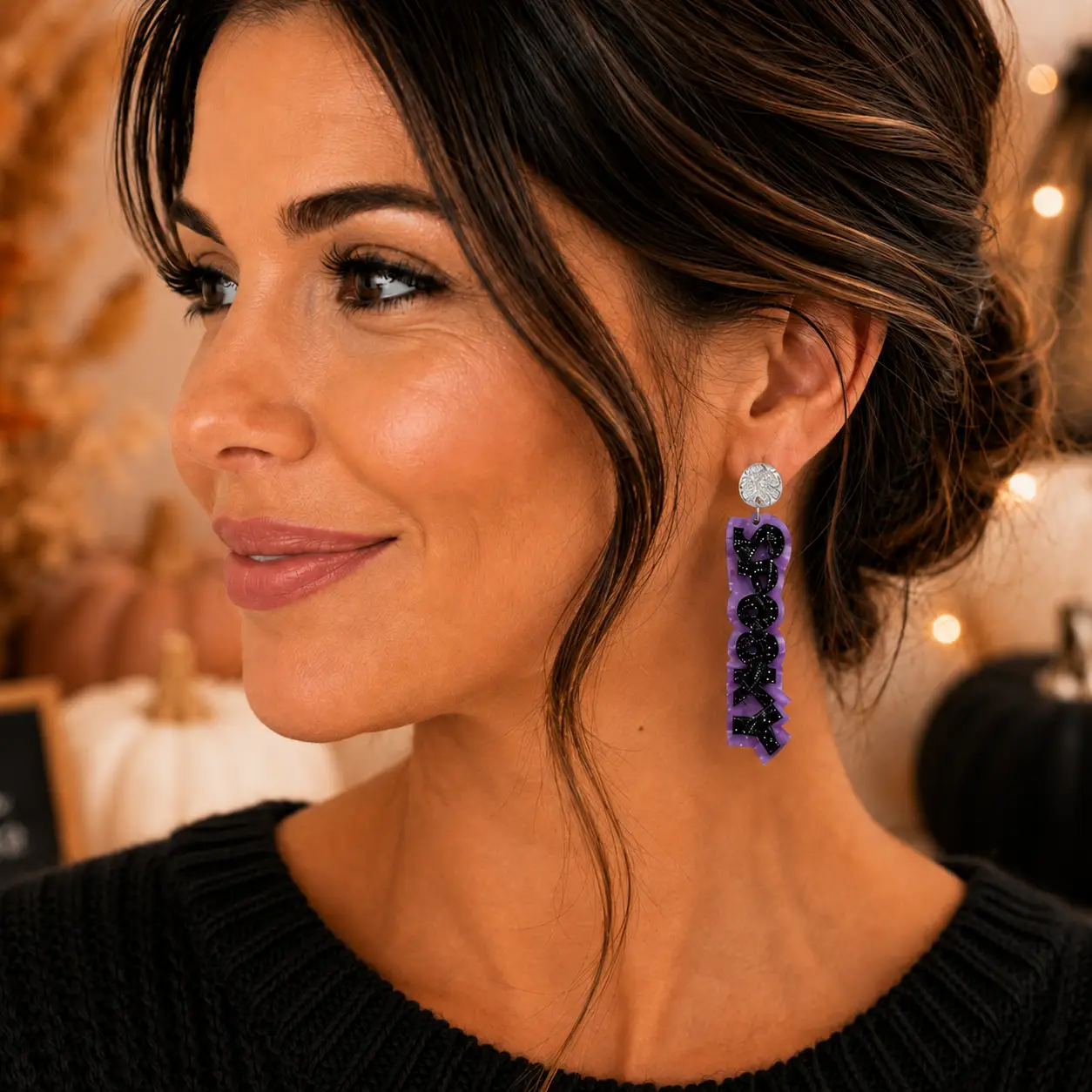 Model wearing long purple SPOOKY Halloween earrings with black glitter lettering and gold-tone hardware in a festive seasonal setting.