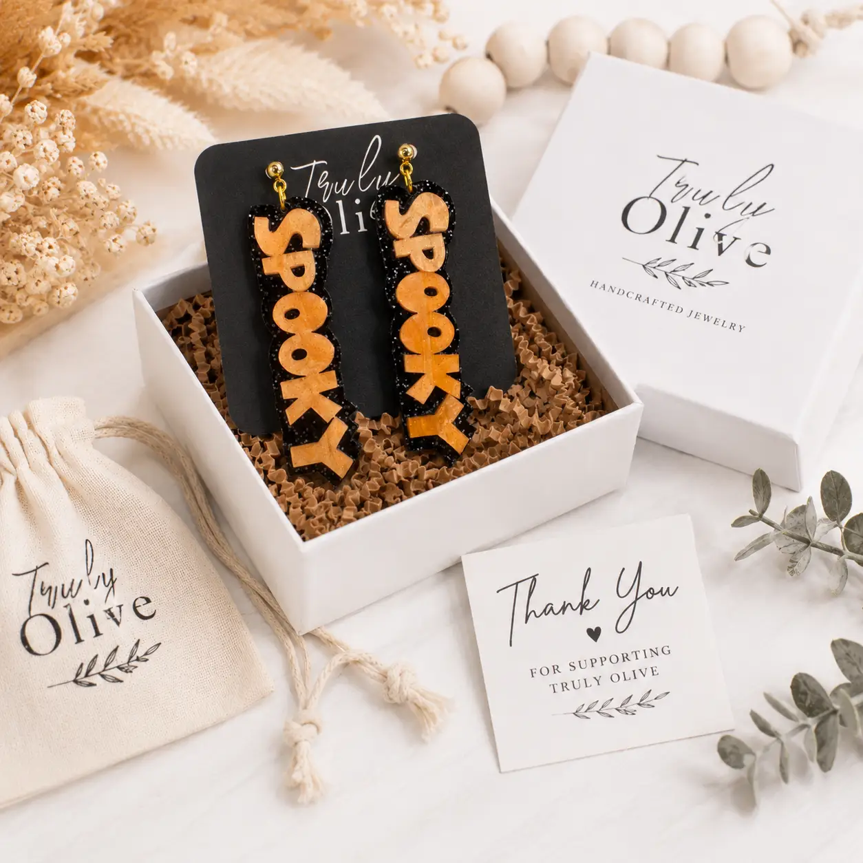 Orange SPOOKY earrings packaged with Truly Olive branding, gift box, pouch, and boutique-ready presentation.