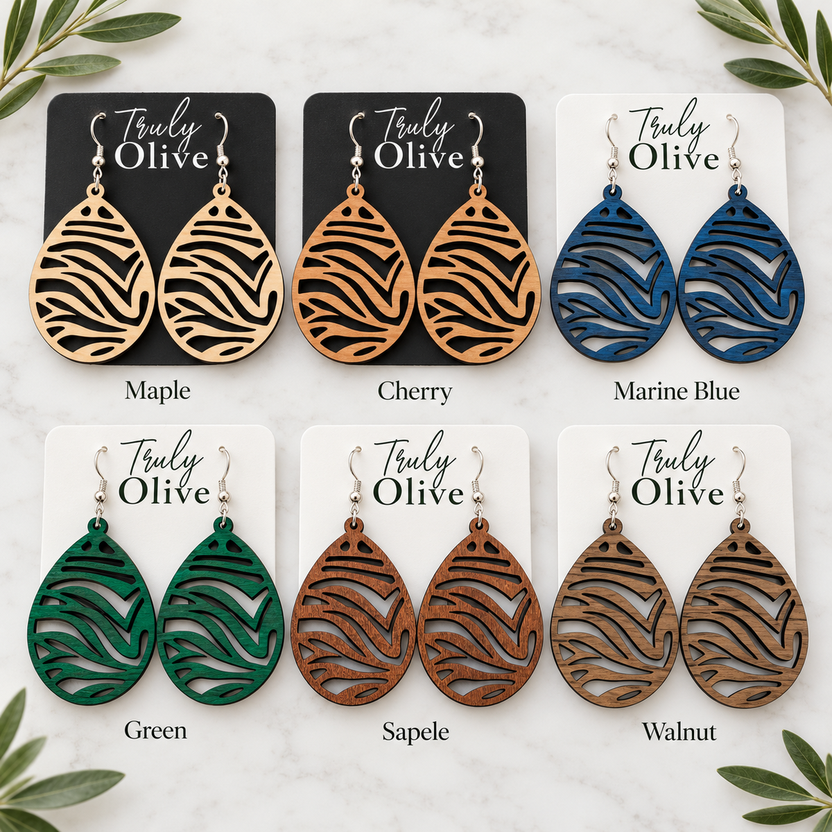Six pairs of zebra cutout wood earrings labeled Maple, Cherry, Marine Blue, Green, Sapele, and Walnut on Truly Olive cards.