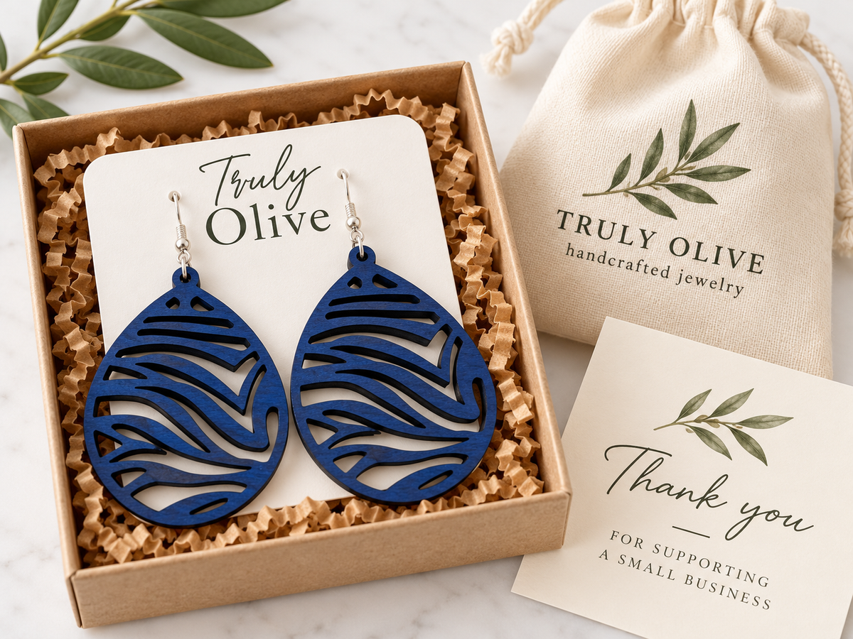 Marine Blue earrings on a white card inside a kraft box, beside a Truly Olive drawstring bag and thank-you card.