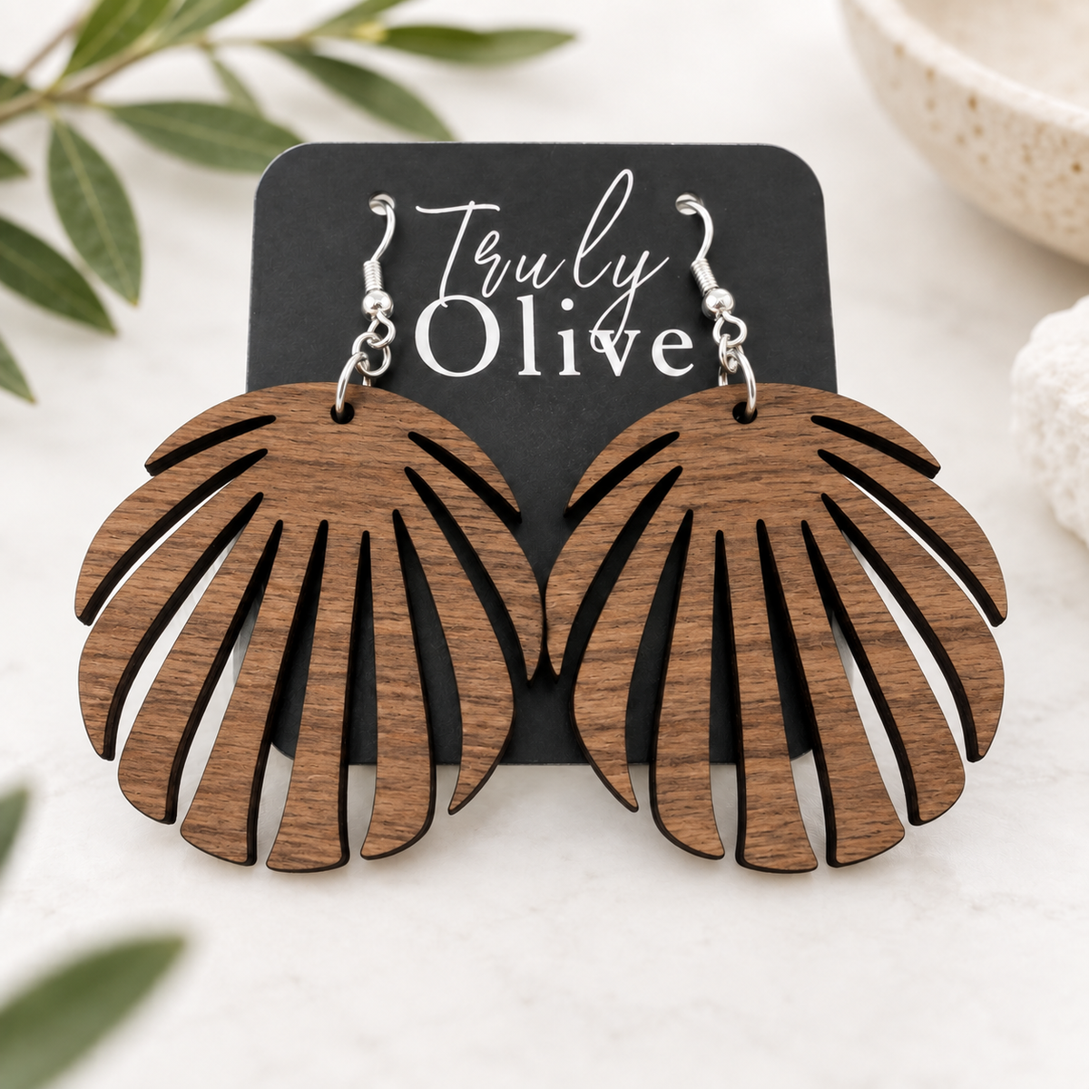 Walnut wood leaf earrings on a Truly Olive card, styled on cream linen with softly blurred greenery.