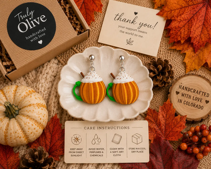 Flat lay of handcrafted pumpkin spice mug earrings with pumpkins, coffee beans, cinnamon sticks, and cozy fall décor, perfect for autumn fashion inspiration.