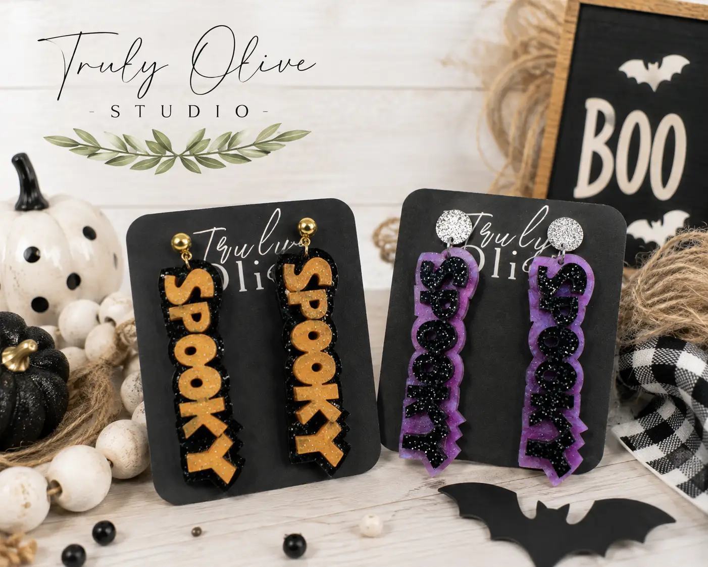 Close-up of layered acrylic SPOOKY earrings showing orange or purple marbled acrylic, black glitter lettering, and textured stud tops.