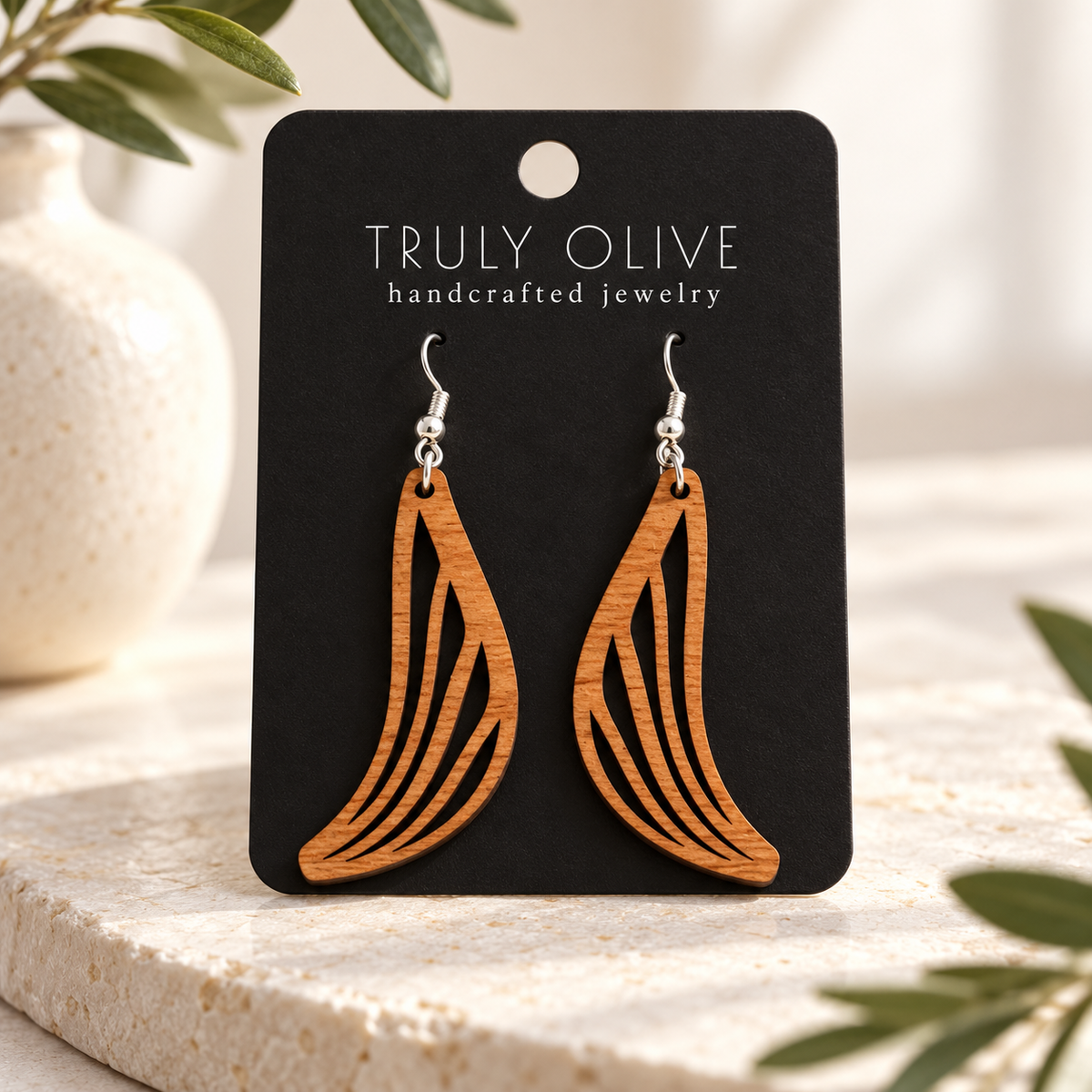 Swept Wing wood earrings in Cherry stain on a black Truly Olive card in a softly lit styled setting.