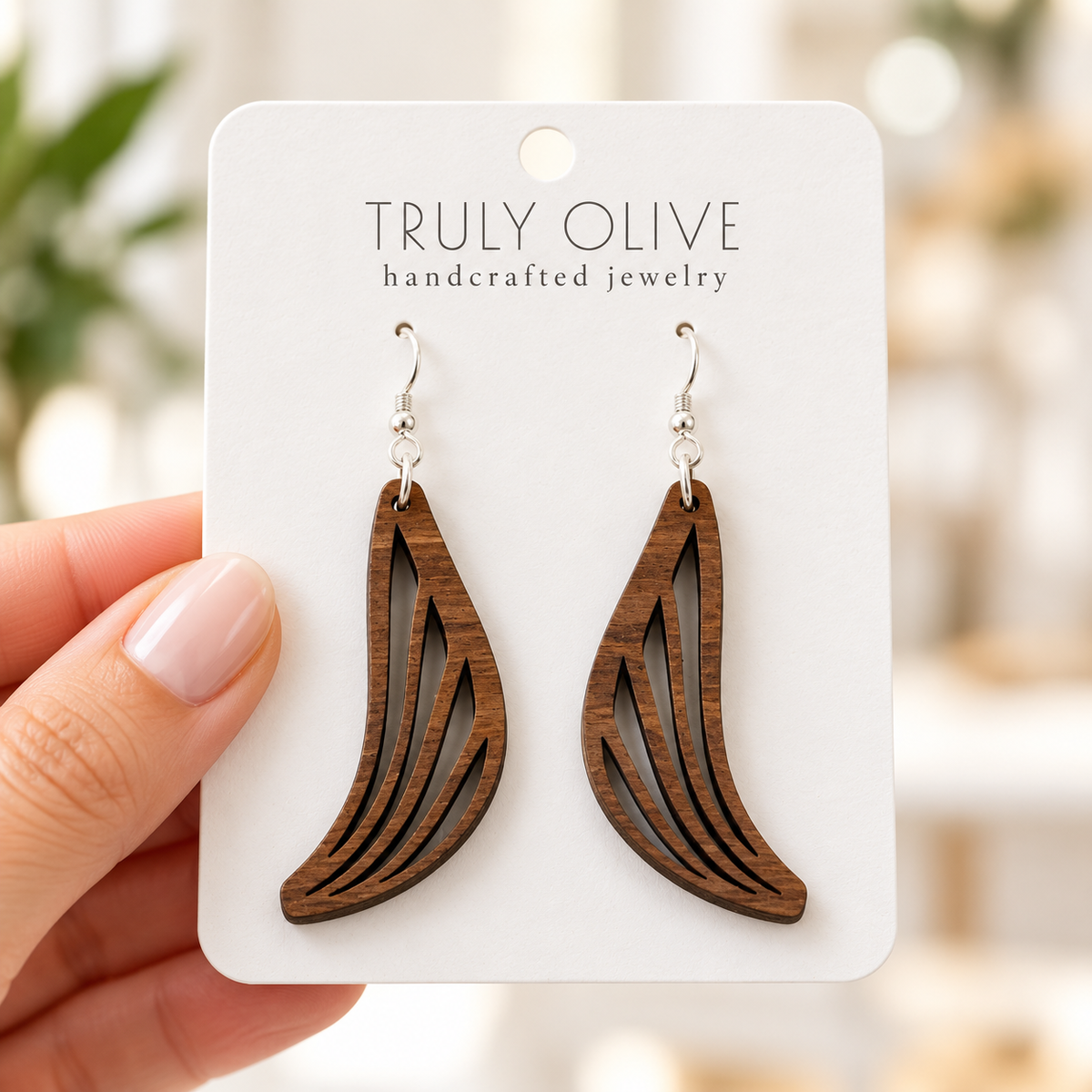 Hand holding a white Truly Olive card with Walnut Swept Wing wood earrings.