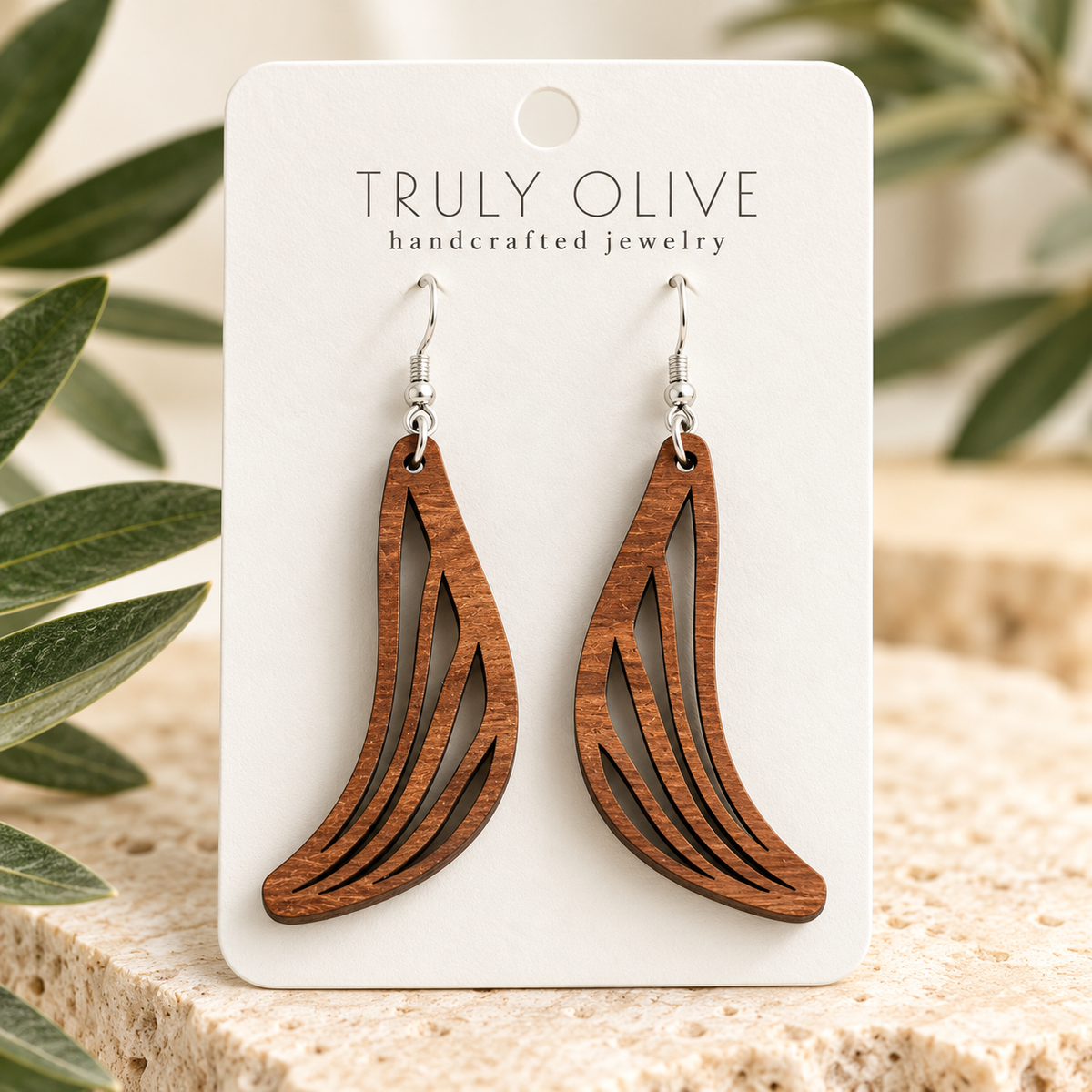 Close view of Sapele Swept Wing wood earrings showing the wood grain and cutout pattern on a white Truly Olive card.