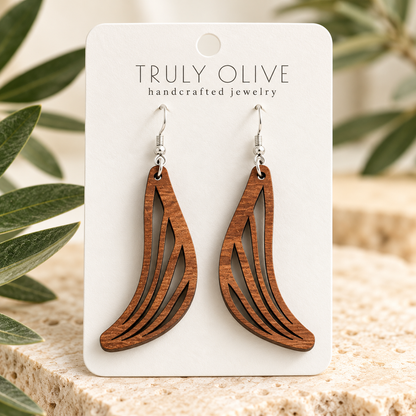 Close view of Sapele Swept Wing wood earrings showing the wood grain and cutout pattern on a white Truly Olive card.