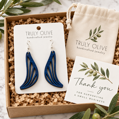 Marine Blue Swept Wing wood earrings on a white Truly Olive card in a kraft box beside a branded pouch and thank-you note.