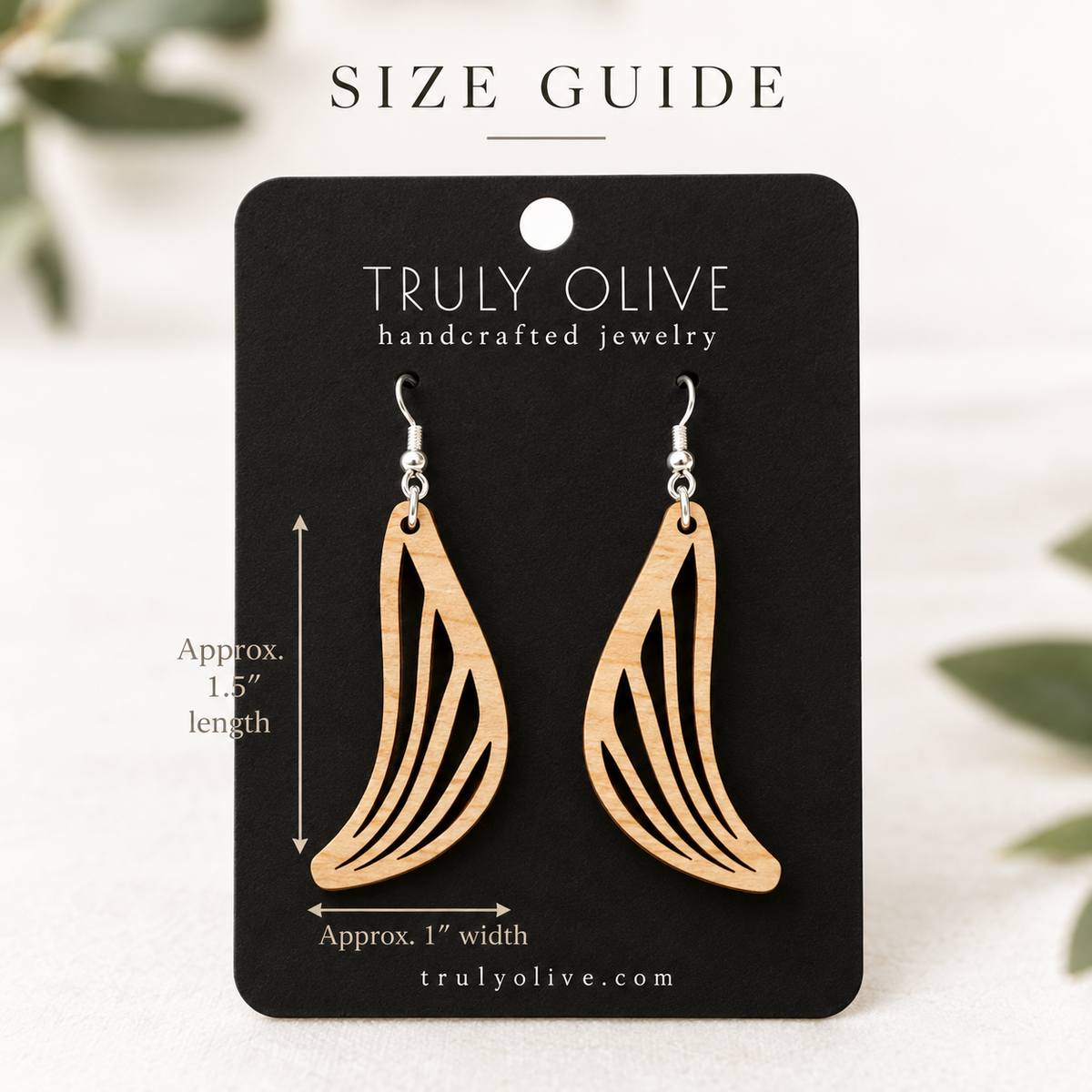 Maple Swept Wing wood earrings on a black Truly Olive card with approximate measurements of 1.5 inches long and 1 inch wide.
