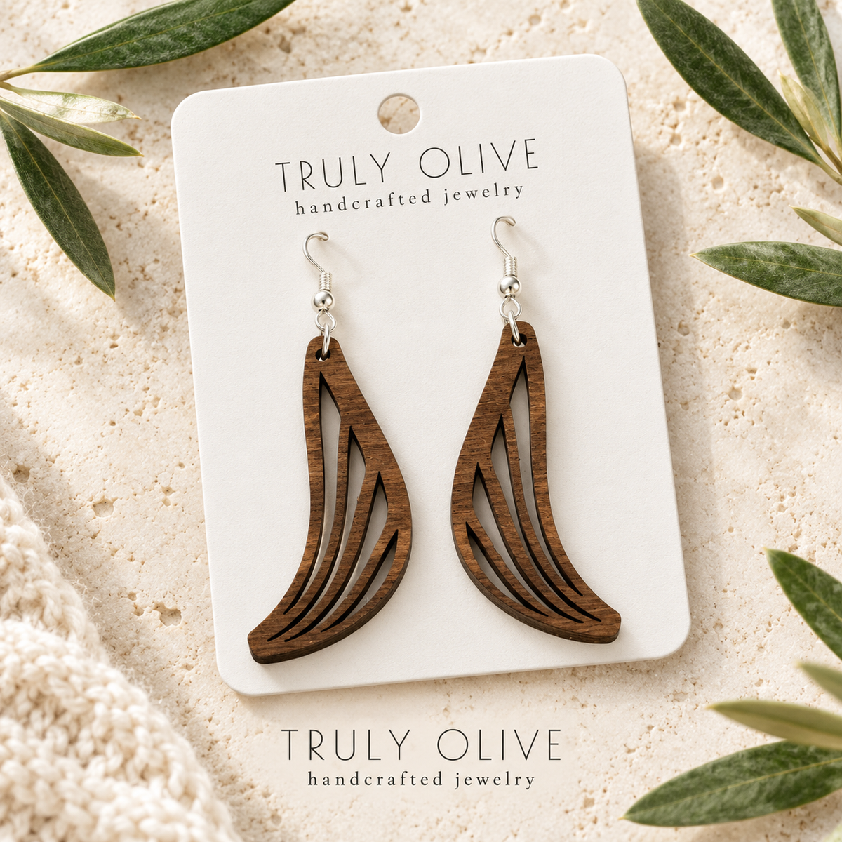 Walnut Swept Wing wood earrings arranged flat with Truly Olive branding.
