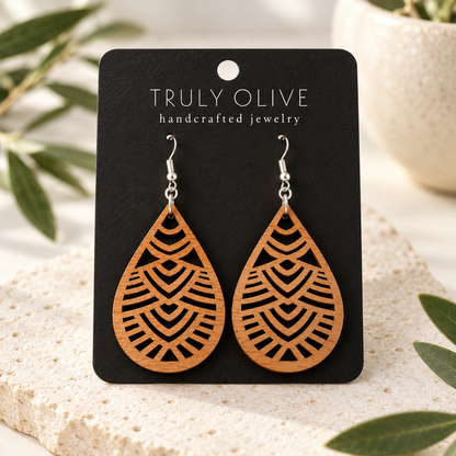 Geometric Teardrop wood earrings in Cherry stain on a black Truly Olive card in a softly lit styled setting.