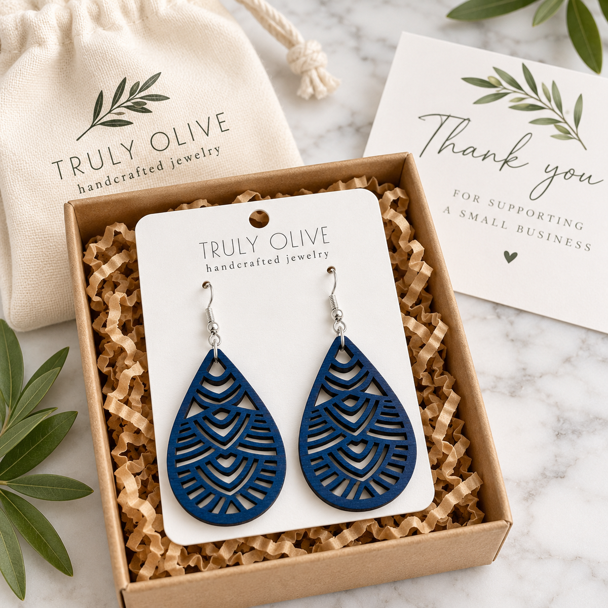 Marine Blue Geometric Teardrop wood earrings on a white Truly Olive card in a kraft box beside a branded pouch and thank-you note.