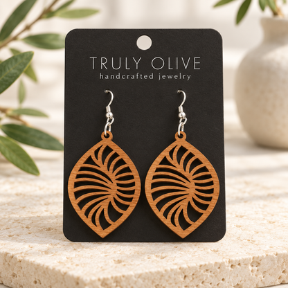 Spiral Leaf wood earrings in Cherry stain on a black Truly Olive card in a softly lit styled setting.