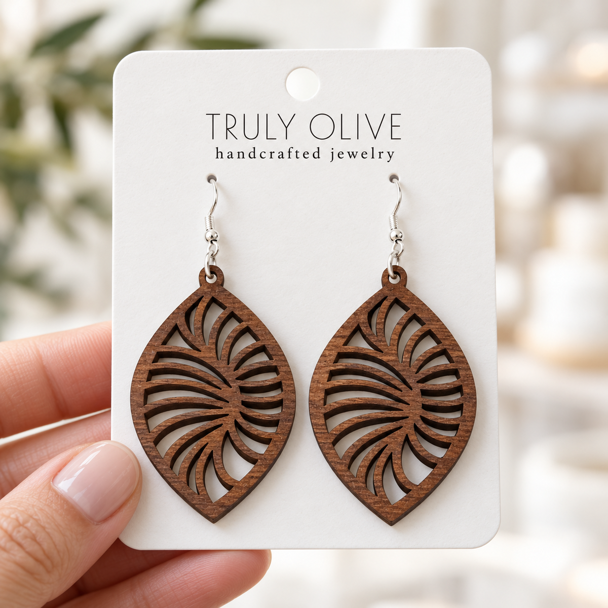 Hand holding a white Truly Olive card with Walnut Spiral Leaf wood earrings.