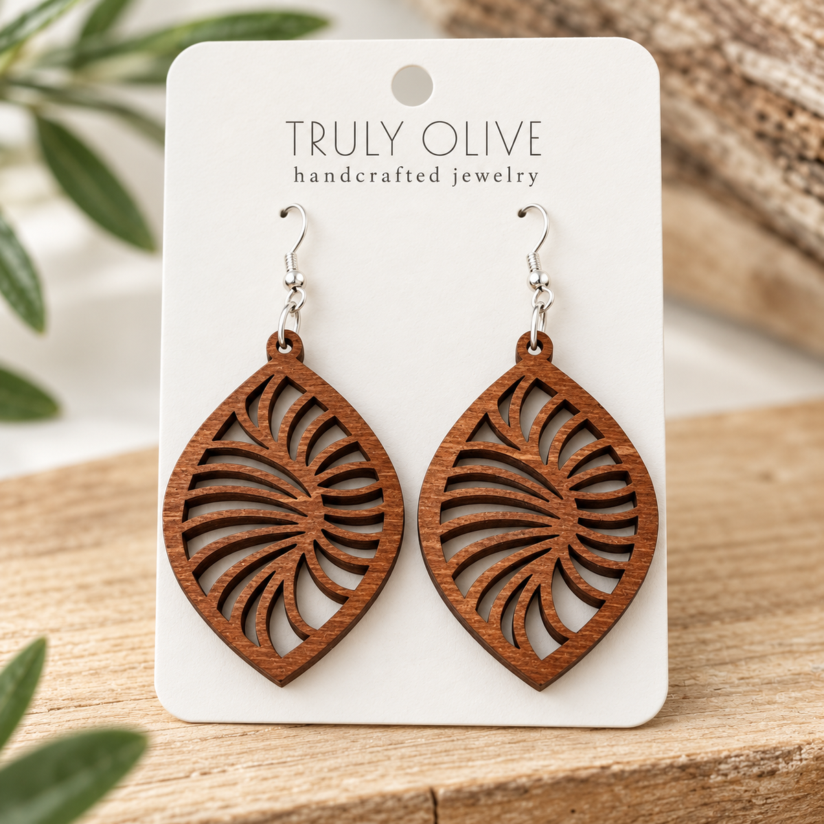 Close view of Sapele Spiral Leaf wood earrings showing the wood grain and cutout pattern on a white Truly Olive card.