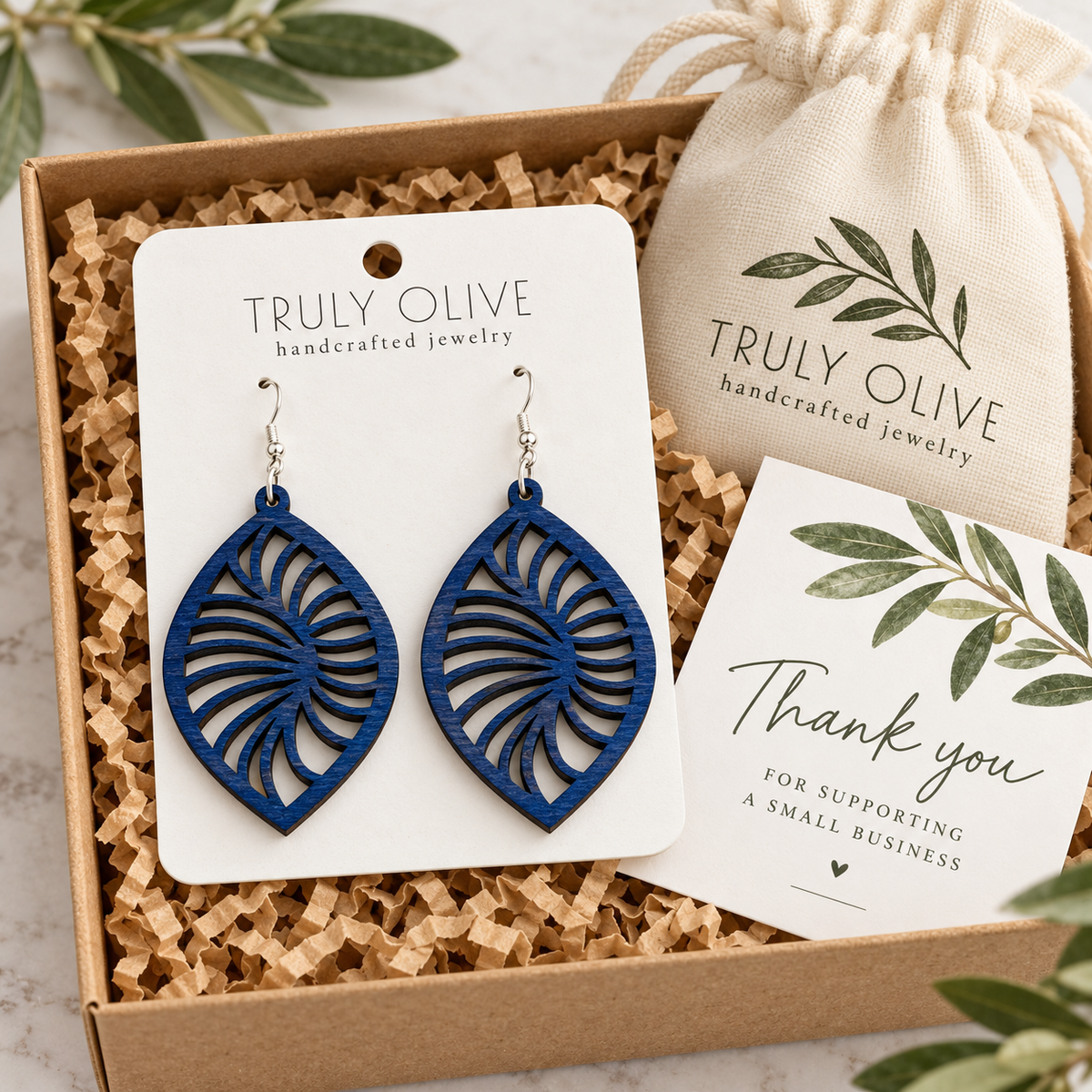 Marine Blue Spiral Leaf wood earrings on a white Truly Olive card in a kraft box beside a branded pouch and thank-you note.