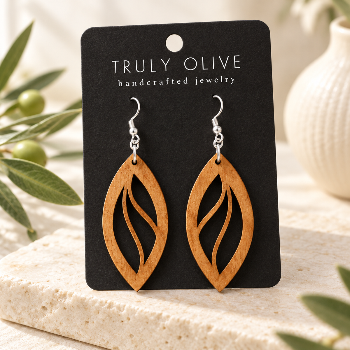 Open Leaf wood earrings in Cherry stain on a black Truly Olive card in a softly lit styled setting.