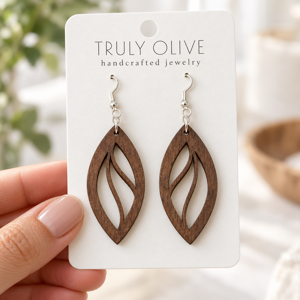Hand holding a white Truly Olive card with Walnut Open Leaf wood earrings.