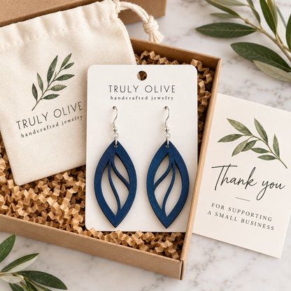 Marine Blue Open Leaf wood earrings on a white Truly Olive card in a kraft box beside a branded pouch and thank-you note.