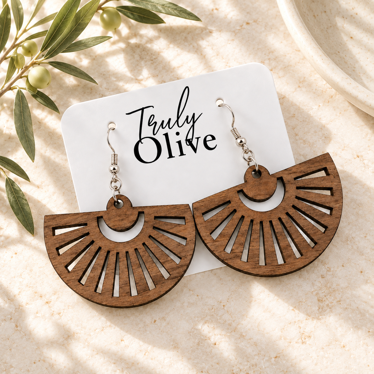 Walnut fan earrings on a white Truly Olive card with olive greenery, photographed overhead.