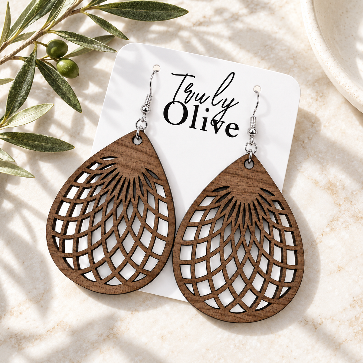 Walnut teardrop earrings on a white Truly Olive card with olive greenery, photographed overhead.