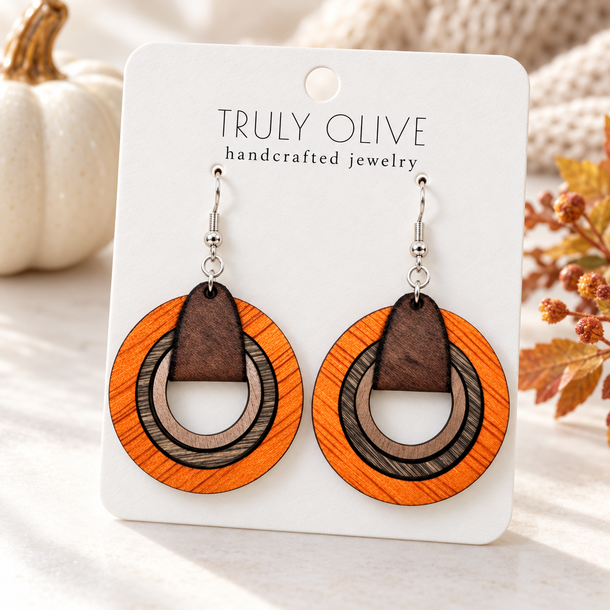 Orange wood hoop earrings on a Truly Olive card styled with a cream pumpkin and warm autumn foliage.