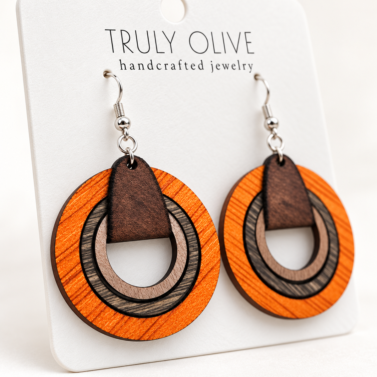 Angled close-up showing the wood grain, nested hoops, and silver-tone hooks of Truly Olive orange earrings.