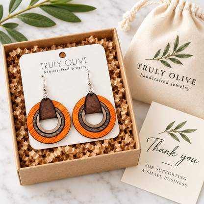Orange wood hoop earrings on an updated Truly Olive card in a kraft box beside a branded pouch and thank-you note.