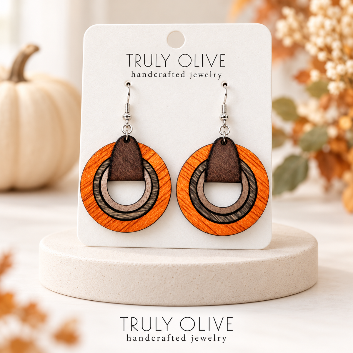 Matching orange wood hoop earrings on a Truly Olive card displayed on an ivory pedestal with autumn accents.