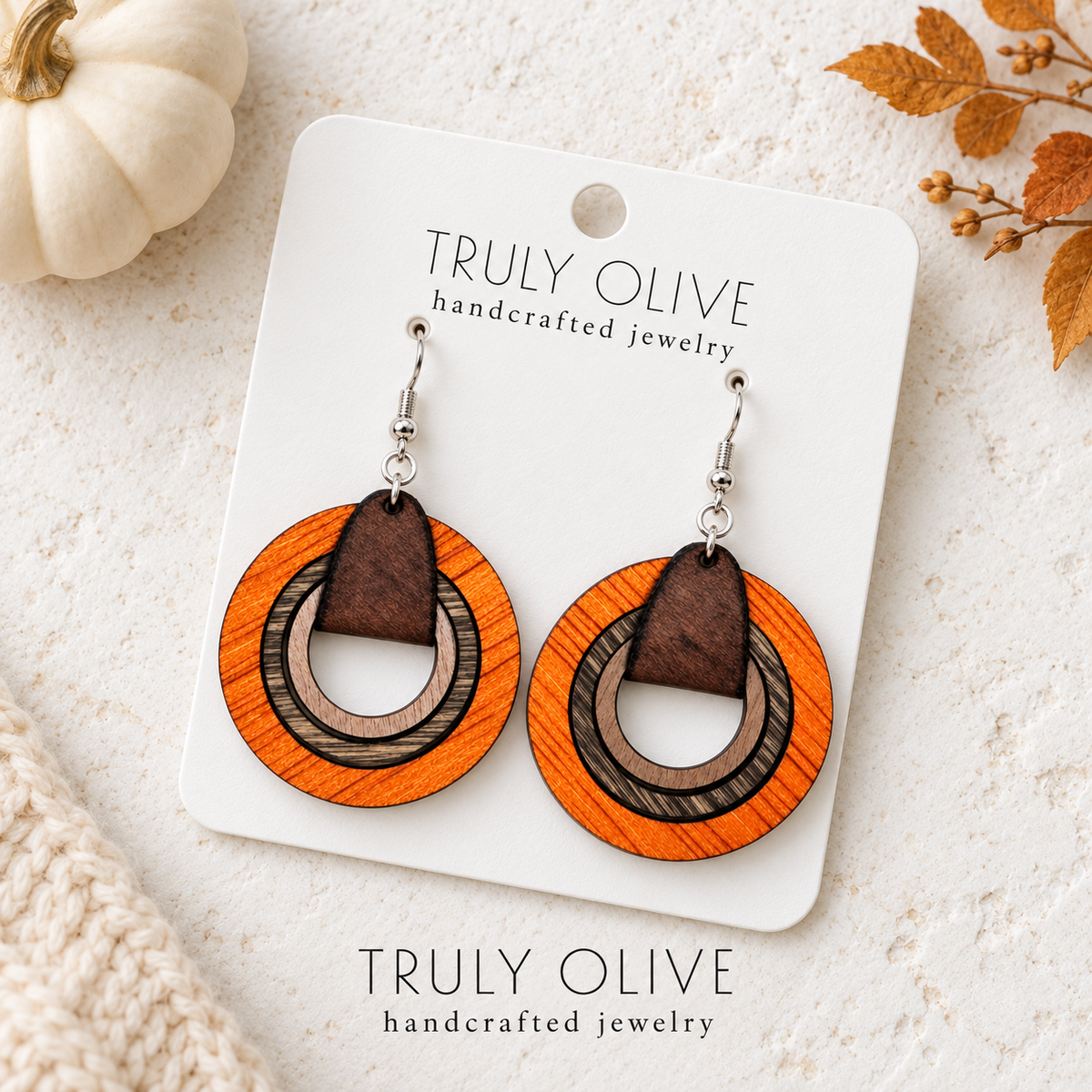 Overhead view of orange wood hoop earrings on a Truly Olive card surrounded by cream and autumn accents.